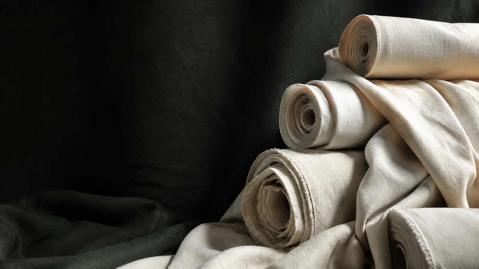 Illustrative ivory fabric rolls against deep green cloth